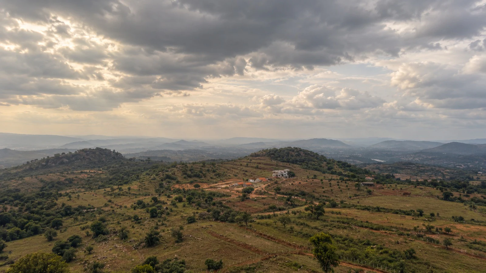 Skyearth from above: green slopes and red earth tracks under a wide cloudy sky, hills fading into the distance